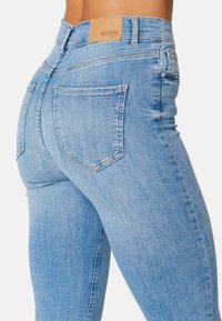 Jasnoniebieskie dżinsy o dopasowanym kroju, z dwoma tylnymi kieszeniami i skórzaną naszywką z logo na pasie. Gładka faktura, bez przetarć.