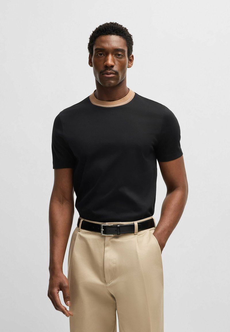 Maglietta nera a maniche corte con colletto a coste beige, abbinata a pantaloni beige e cintura nera. Tessuto liscio con design aderente.