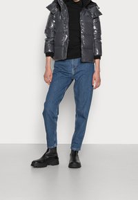 Szary, błyszczący kurtka puchowa z kapturem, czarna koszulka z długim rękawem, jasnoniebieskie dżinsy i czarne, masywne botki za kostkę. Gładkie faktury i luźny krój.