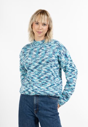 Pulover tricotat în nuanțe de albastru, cu guler înalt, mâneci lungi și un model texturat în zigzag. Asociat cu blugi cu talie înaltă.