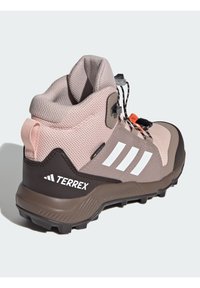 Svijetlo ružičasta i smeđa planinarska čizma s mrežastim gornjim dijelom, gumeni potplat, teksturirani detalji i bijeli logo. Ima sustav za sigurno zaključavanje vezica.