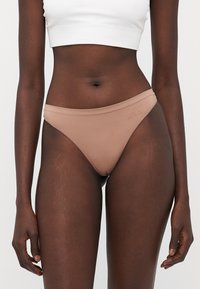 Nude sømløse bikini-truser med en glatt tekstur, lav midje-design og subtil logo-detalj på linningen.