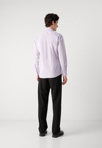 Cămașă lungă de culoare lila, cu o croială ajustată, asortată cu pantaloni negri, văzută din spate. Material neted și mansete cu nasturi.