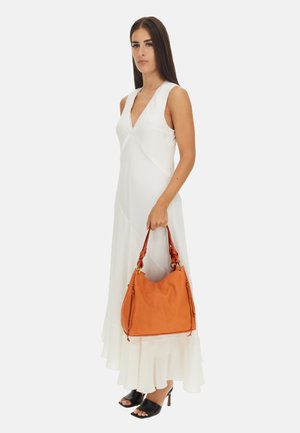 Borsa in pelle arancione con un design morbido. Presenta una parte superiore curva, un fondo strutturato e manici intrecciati. Indossata da un modello in un vestito bianco.