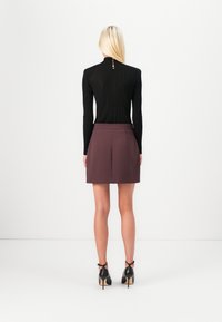 Black ribbed long-sleeve top with high neck and five gold buttons at the back, paired with a short burgundy skirt and black high-heeled shoes.