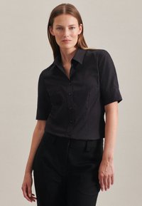 Camicia nera a maniche corte con bottoni e colletto a punta, caratterizzata da una texture di tessuto liscia e un design aderente.