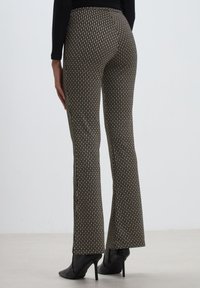 Pantalons évasés avec un motif noir et beige, ayant une surface texturée, dotés d'une taille haute et d'une coupe ajustée jusqu'aux chevilles.
