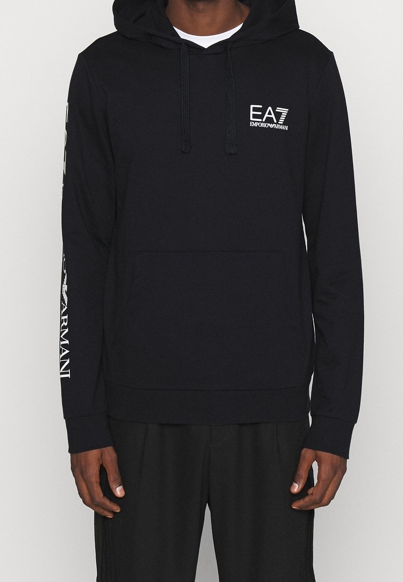 Sudadera con capucha negra hecha de tejido suave, que cuenta con un bolsillo frontal, cordones y una marca en el pecho y la manga.