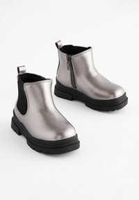 Metallische silberne Knöchelboots mit schwarzen elastischen Seiteneinsätzen, Reißverschluss und einer klobigen schwarzen Sohle. Glatte Textur mit minimalen Akzentdetails.
