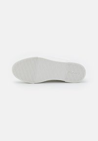 Semelle de sneaker blanche avec des rainures horizontales et verticales pour une meilleure traction. Présente un design minimaliste avec un logo de marque en relief près du talon.