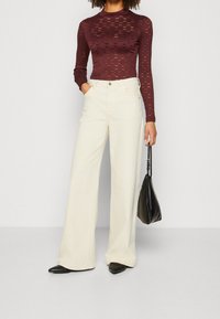 Burgundy stickad långärmad topp med ett bikake-mönster, kombinerad med högmidjade, vida vita byxor och en svart handväska.