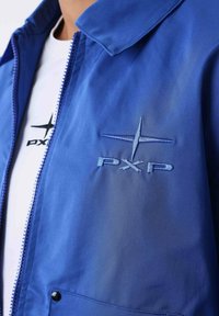 Blå jakke med en glat tekstur, prydet med et broderet "PXP" logo. Den har lynlås foran, spids krave og en lomme med trykknaplukning.
