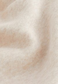 Tissu beige clair avec une texture douce, affichant des variations subtiles de couleur et un motif de tricot fin, drapé pour montrer des plis et des contours.