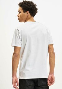 Hvid bomuld t-shirt med korte ærmer og rund halsudskæring, set fra ryggen, parret med mørke jeans. Glat tekstur og enkel design.