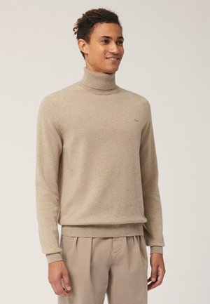 Maglione beige a collo alto in morbido tessuto a maglia, con maniche lunghe e polsini a costine. Piccolo logo sul petto, texture liscia.