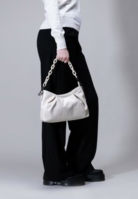 Cream-colored leather handbag with a pleated design and a chain strap. Displayed next to black wide-leg trousers and chunky black shoes.