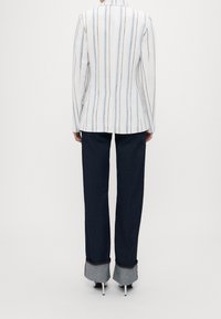 White and blue striped blazer with a tailored fit, paired with dark denim pants featuring a folded light gray cuff.