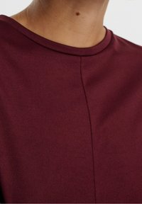 Burgundy paita, jossa on pyöreä kaula-aukko ja lyhyet hihat, ominaisuutenaan sileä, teksturoitu kangas ja keskisaumadetail.