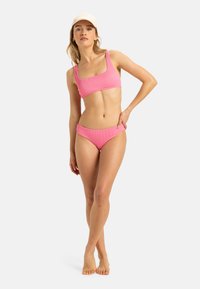 Pink ribbed bikini set featuring a square neckline top and low-rise bottoms, with a smooth texture and minimalistic design.
