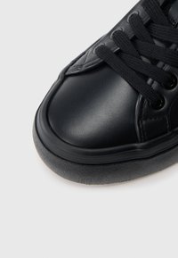 Pantof sport negru cu partea superioară din piele netedă, vârf rotund, șireturi negre și talpă de cauciuc cu finisaj texturat.