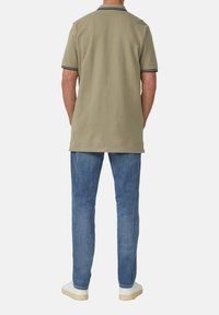 Oliwkowa koszulka polo z kołnierzem i granatowymi paskami przy dekolcie, w połączeniu z jasnoniebieskimi dżinsami i białymi trampkami.