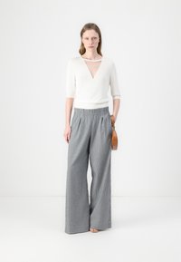 White knitted top with a V-neck and short sleeves, paired with wide-leg gray striped trousers and a small brown handbag.
