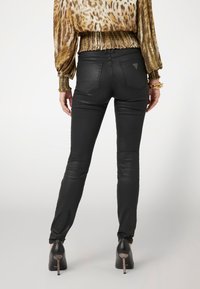 Pantalones ajustados de cuero negro con una textura suave, que cuentan con dos bolsillos traseros y un pequeño detalle de logo. Llevados con zapatos de tacón alto.