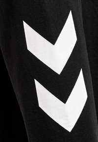 Dwie białe strzałki typu chevron skierowane w dół na czarnym tle z tkaniny, prawdopodobnie część ubrania.