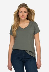 T-shirt à col en V à manches courtes en vert olive, fabriqué à partir d'un tissu doux avec une coupe décontractée. Porté avec un jean bleu foncé, mettant en avant un style décontracté.