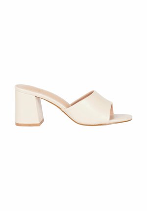 Mule beige con punta aperta, cinturino largo e tacco a blocco, mostrato di lato su sfondo bianco.
