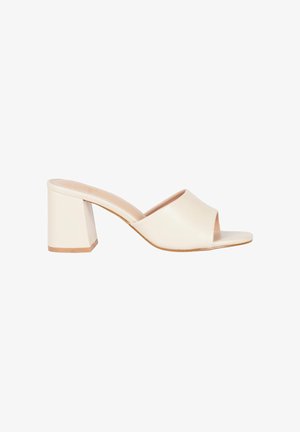 Mule beige con punta aperta, cinturino largo e tacco a blocco, mostrato di lato su sfondo bianco.
