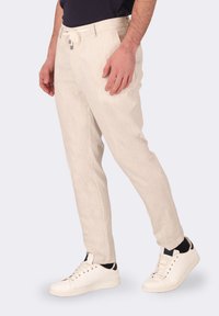 Pantaloni beige chiaro con una finitura testurizzata, vita con cordoncino e vestibilità affusolata, abbinati a sneakers bianche.