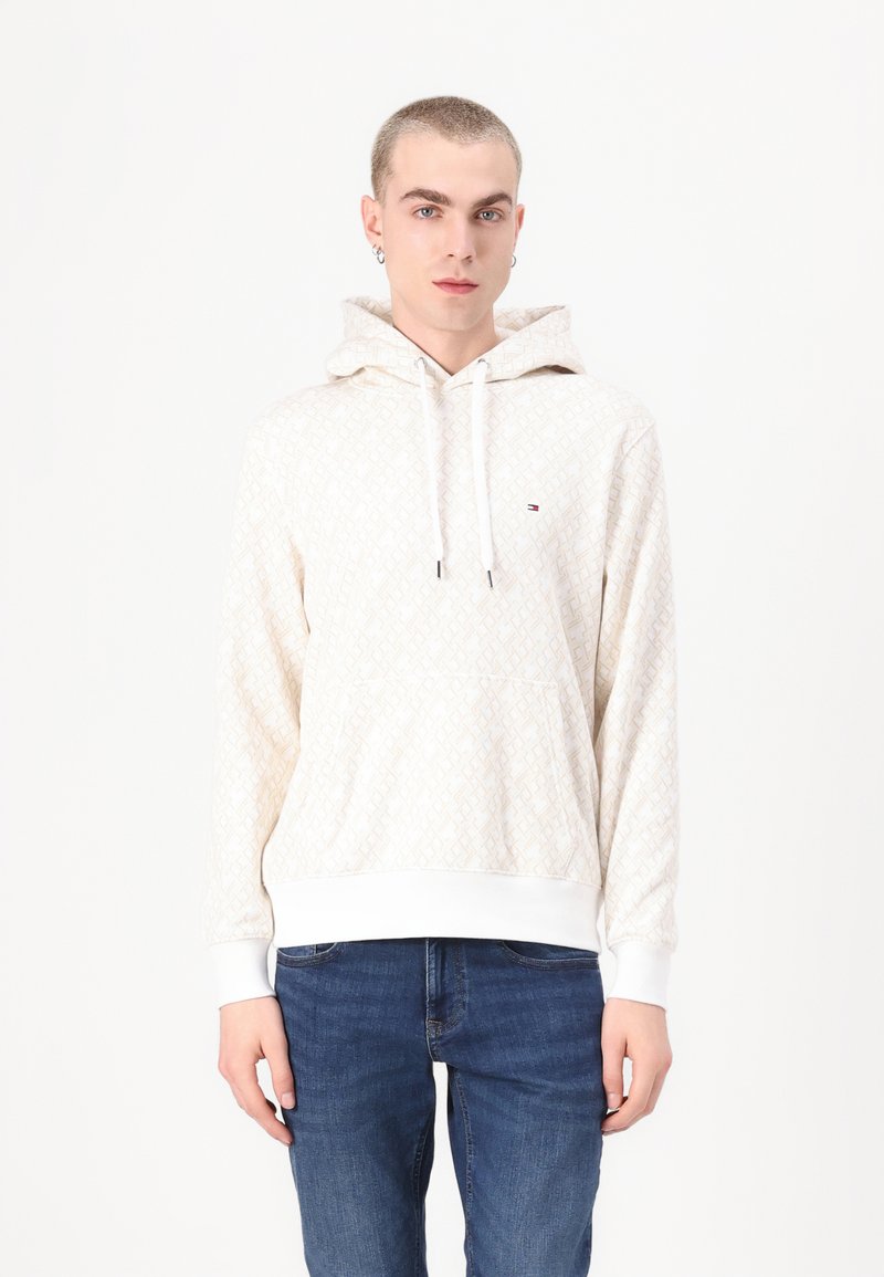 Kapuzensweatshirt in Creme mit geometrischem Muster, ausgestattet mit einer vorderen Kängurutasche, weißen gerippten Bündchen und einem kleinen Logodetail.