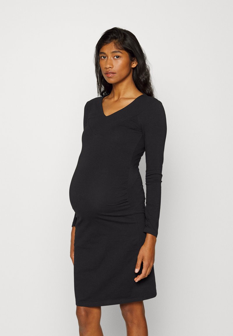 Vestido de maternidade preto de mangas longas com decote em V, forma ajustada e franzidos nas laterais, feito de um tecido elástico e suave.