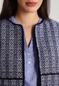 Giacca a motivo navy presenta una trama testurizzata con un design decorativo, abbinata a una camicia azzurro chiaro con accenti sottili.