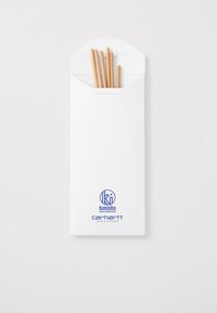 Des baguettes en bois brun dans une enveloppe blanche avec un rabat arrondi, ornées de logos imprimés en bleu pour Kuumba International et Carhartt.