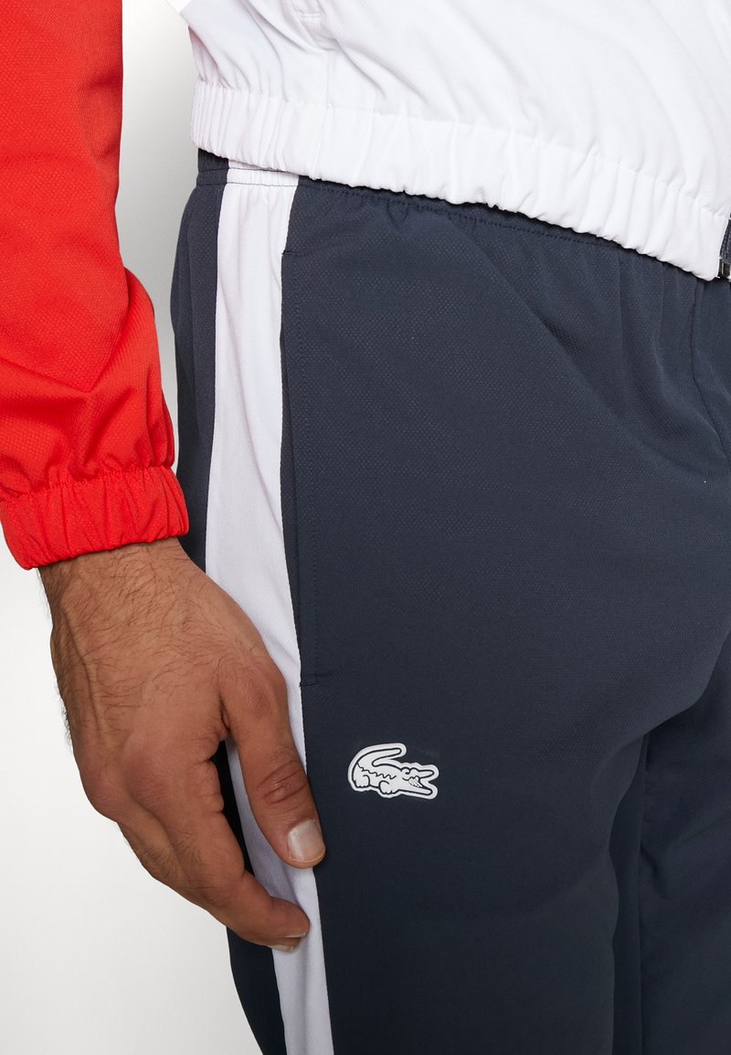 Pantaloni sportivi navy con strisce laterali bianche e logo ricamato. Realizzati in tessuto traspirante con vita elastica e tasche.
