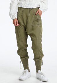 Persona que lleva unos pantalones cargo jogger en verde oliva con grandes bolsillos y cordones, combinados con zapatillas blancas y una camiseta blanca de manga larga.