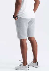 Shorts rayés gris avec une coupe décontractée, poches latérales, associés à des baskets blanches perforées. Les shorts ont une texture lisse et une coupe à hauteur des genoux.
