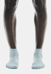 Calcetines tobilleros de color azul claro con puños acanalados, llevados sobre piernas oscuras, que presentan una textura suave y un diseño minimalista.