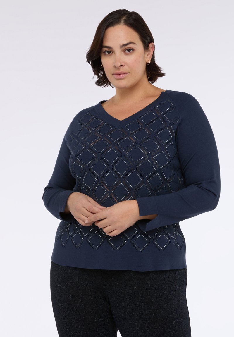 Námořnický modrý svetr s výstřihem do V a dlouhými rukávy. Obsahuje diamantový vzor s výřezy a malými ozdobami po celé přední části.