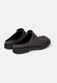 Zapatos grises tipo slip-on con un upper suave y texturizado y una suela negra duradera. Forma redondeada con un tacón bajo y sin cordones ni acentos de hardware visibles.