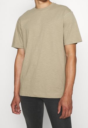 Beige T-Shirt mit kurzen Ärmeln aus weicher Baumwolle, mit klassischem Rundhalsausschnitt und entspannter Passform. Nahtdetails an den Schultern.