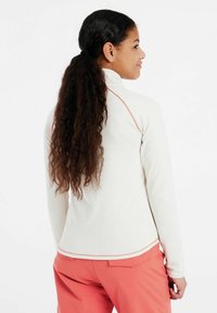 Pullover chiaro a maniche lunghe con colletto alto, caratterizzato da accenti corallo e una superficie liscia, indossato con pantaloni rosa.