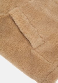 Tessuto in pelliccia artificiale color beige caratterizzato da una texture morbida e pelosa con una superficie liscia. Il materiale presenta una tonalità uniforme e senza motivi visibili.