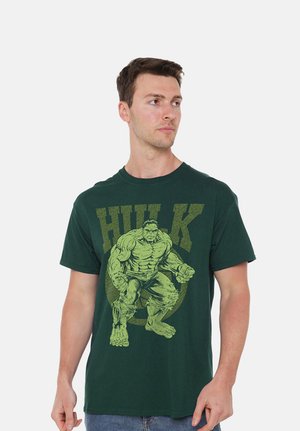 Man wearing dark green T-shirt with a large graphic of the Hulk character and "HULK" text, looking to his left.