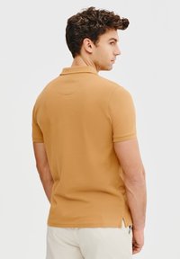 Koszulka polo w musztardowym kolorze, krótki rękaw, dzianinowy materiał, z bocznymi rozpórkami i klasycznym kołnierzykiem. Gładka tekstura; minimalistyczny design.