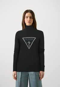 Mustvalge särk, millel on kolmnurkne "GUESS" logo hõbedaste detailidega. Kangas on sile, pikkade varrukatega ning kehakujuline.