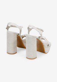 Beige platform sandals with block heels, featuring a suede-like texture, open toe design, and adjustable ankle strap with a buckle.