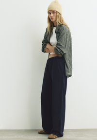 Casualny strój złożony z koszuli w kratę, białej bluzki crop top, granatowych spodni o szerokich nogawkach oraz brązowych butów wsuwanych ozdobionych wstawkami w postaci ćwieków.